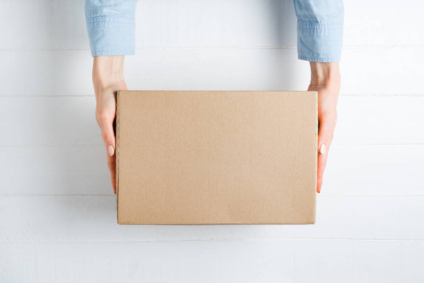 Прямоугольная картонная коробка в женских руках. Вид сверху, белый фон
 - Фото, изображение