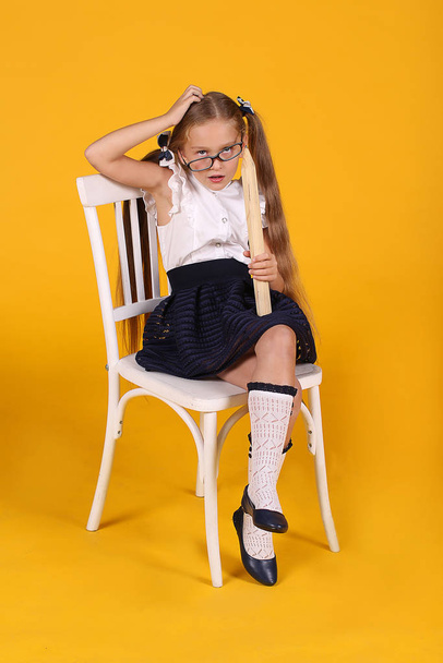 Girl-student in a white wooden chair in glasses with cool facial expressions with a huge pencil in her hands on a yellow background - Photo, image