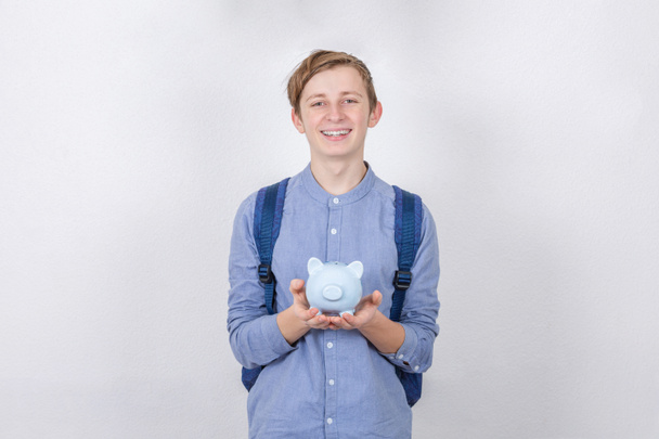 Smiling Teenager boy holding piggy bank over white background. F - 写真・画像