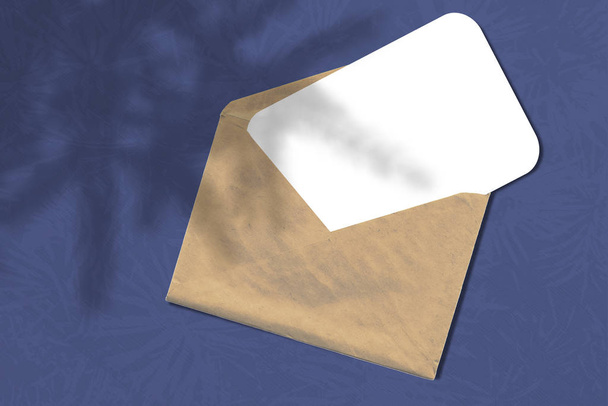 Umschlag mit einem Blatt Papier auf blauem Hintergrund. Layout mit der Auferlegung des Weihnachtsbaumschattens. natürliches Licht wirft Schatten von oben. - Foto, Bild
