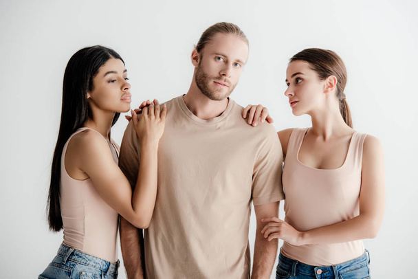 young multicultural women standing near handsome man in beige outfit isolated on white - Φωτογραφία, εικόνα