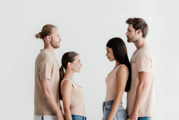 side view of young multicultural men and women in beige outfit standing face to face isolated on white - Valokuva, kuva