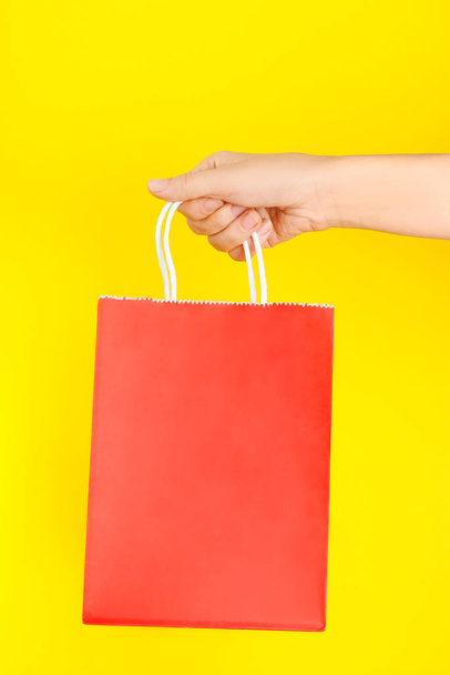 Hand holding red shopping or gift bag against yellow background - Valokuva, kuva
