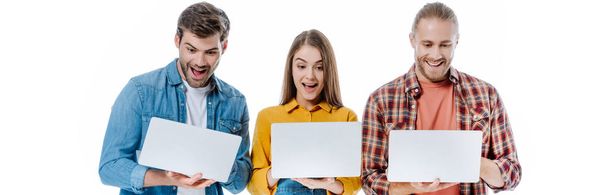 heureux jeunes amis tenant des ordinateurs portables avec les bouches ouvertes isolé sur blanc, panoramique coup
 - Photo, image