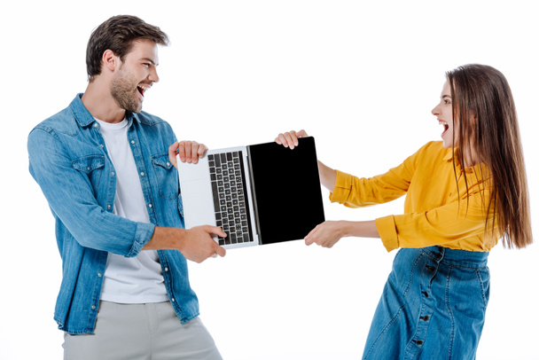 θυμωμένο νεαρό ζευγάρι ουρλιάζοντας ενώ μοιράζονται φορητό υπολογιστή απομονωμένο σε λευκό - Φωτογραφία, εικόνα