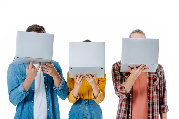 τρεις νεαροί φίλοι κρατώντας φορητούς υπολογιστές μπροστά από το πρόσωπο απομονώνονται σε λευκό - Φωτογραφία, εικόνα