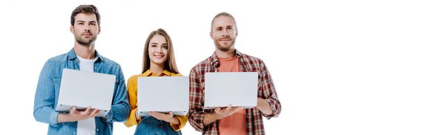 Lächelnd halten drei junge Freunde Laptops isoliert auf weißen, panoramischen Aufnahmen - Foto, Bild