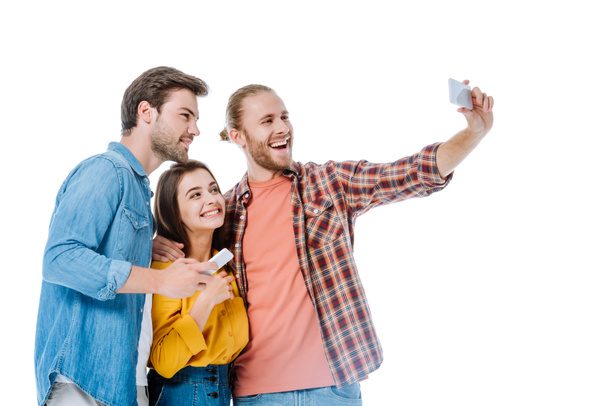smiling three young friends taking selfie on smartphone isolated on white - 写真・画像