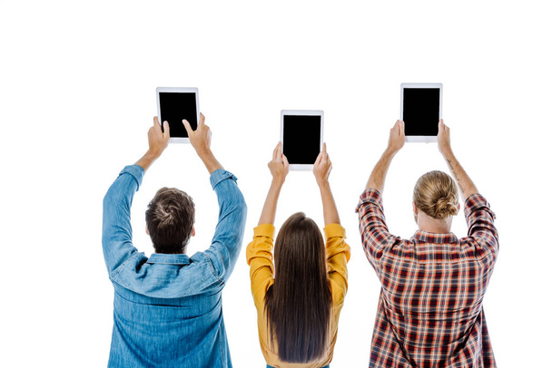 vista posterior de tres jóvenes amigos sosteniendo tabletas digitales con pantallas en blanco aisladas en blanco
 - Foto, Imagen