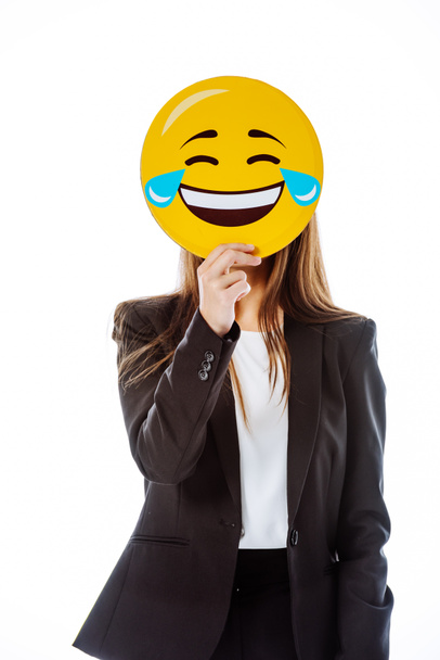 KYIV, UKRAINE - AUGUST 12, 2019: businesswoman in suit holding Face With Tears of Joy emoji in front of face isolated on white - Foto, Imagen