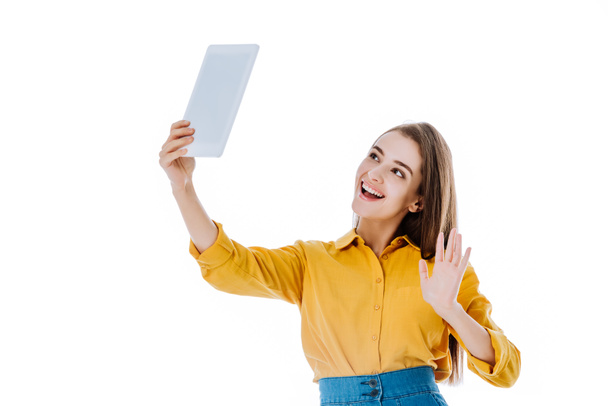 uśmiechnięta atrakcyjna dziewczyna machająca ręką podczas rozmowy wideo na tablecie cyfrowym odizolowana na biało - Zdjęcie, obraz