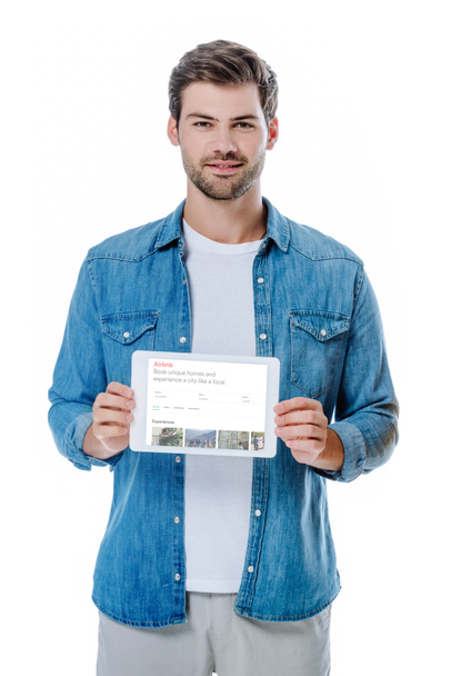 KYIV, UCRAINA - 12 AGOSTO 2019: camicia uomo in denim sorridente con tablet digitale e pagina airbnb isolata su bianco
 - Foto, immagini