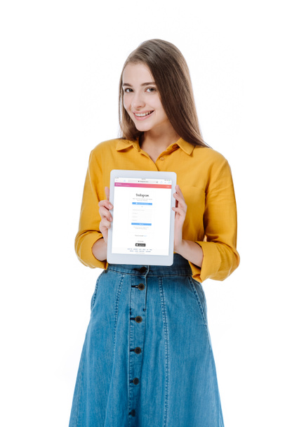 KYIV, UKRAINE - AUGUST 12, 2019: smiling girl in denim skirt holding digital tablet with Instagram app isolated on white - Fotografie, Obrázek