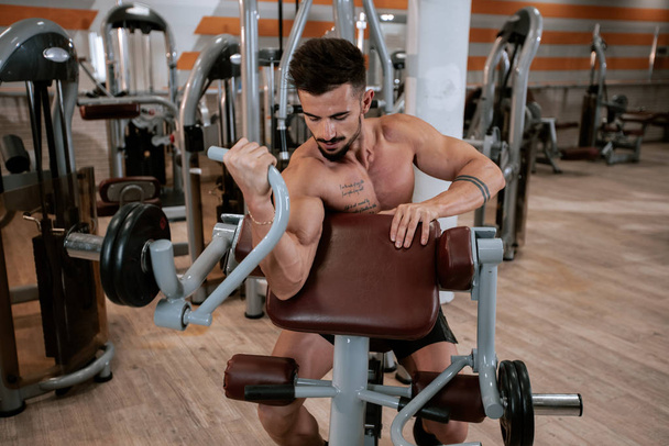 Λεπτομέρειες bodybuilding άνθρωπος κάνει ασκήσεις σε ένα μεγάλο ευρύχωρο γυμναστήριο πορτραίτο ψημένα δικέφαλους προπόνηση ανύψωση του κούφος - Φωτογραφία, εικόνα