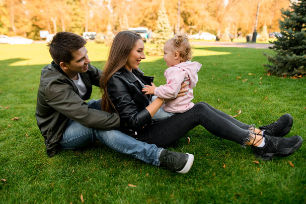 Happy family sitting on the green lawn with a baby on the mother knees - Photo, Image