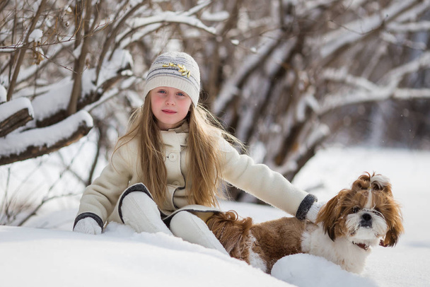 child plays with his pet on Christmas holidays in forest. Beautiful girl smiles, caresses her beloved dog in winter in park. - Fotografie, Obrázek