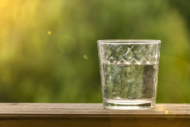 glas water op een houten tafel achtergrond van groene bokeh - Foto, afbeelding