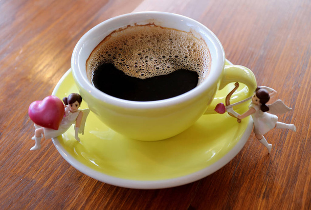 Чашка усміхненої форми чорної кави з двома милими міні, куполоподібна фігурка дівчини на дерев'яному столі
 - Фото, зображення