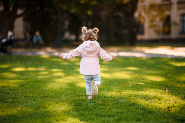 Cute little girl running in the park on the green grass - Fotó, kép
