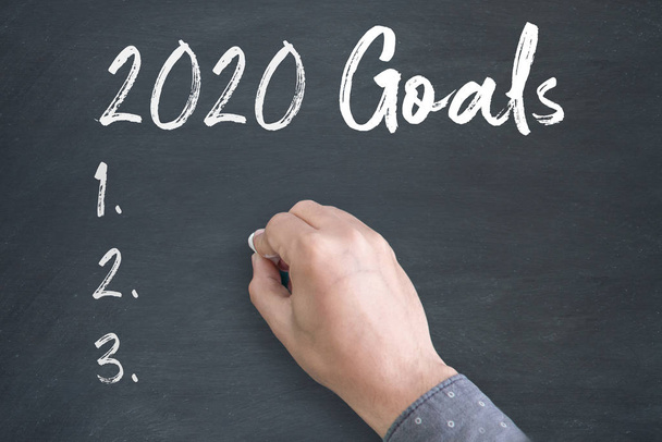 Young Man standing below blackboard with chalk drawing of new year 2020 Goals - Photo, Image