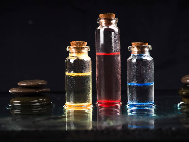 Три барвисті рідкі скляні флакони з чорним фоном для медичних досліджень. У хімічній лабораторії Скляний флакон з пробкою чорного кольору. Кілька скляних флаконів з пробкою
 - Фото, зображення