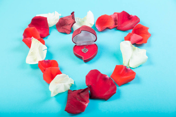 Heart of rose petals on a blue background and a heart-shaped box with jewelry. - Фото, зображення