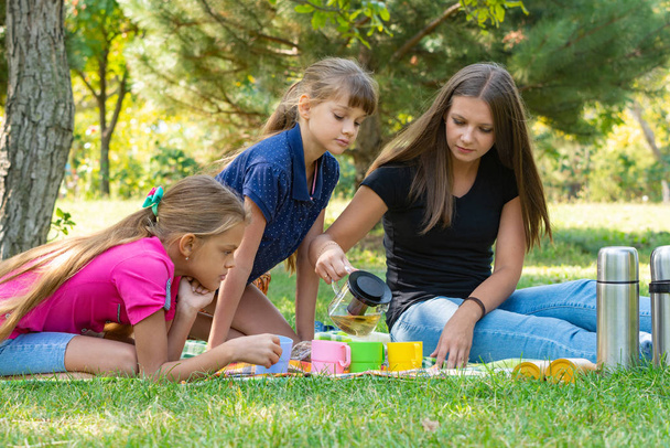 Familie op een picknick, meisje schenkt thee in glazen - Foto, afbeelding