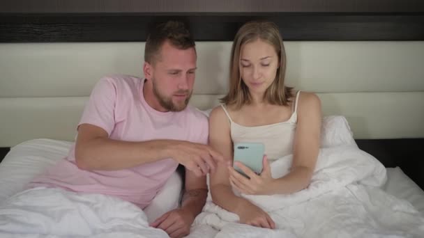Young couple surfing internet on mobile lying in bed - Felvétel, videó
