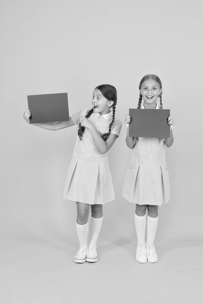 Delivering fresh information. Announcement and promotion. Schoolgirls cheerful pupils informing you. Girls school uniform hold posters. Back to school. School girls hold blank paper copy space - Foto, Imagem