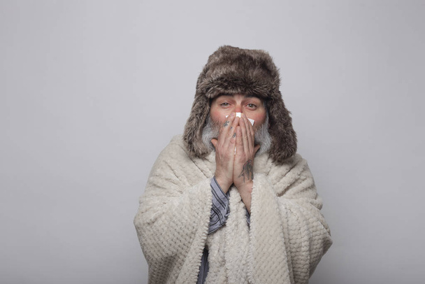 mature man covering himself with a blanket and hat blowing his n - Фото, изображение