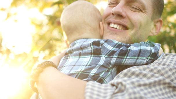 幸せな若い父親は秋の公園で彼の2歳の息子を抱きしめる。男は喜んで笑って、父の日、近い肖像画 - 映像、動画