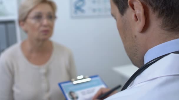 Male doctor checking female patient medical history form, health examination - Metraje, vídeo