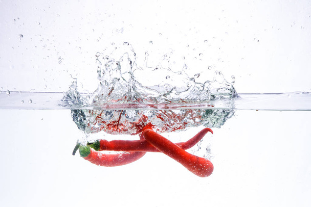 hot chili pepper in the water. splash of water and fruit floating in it. - Foto, afbeelding
