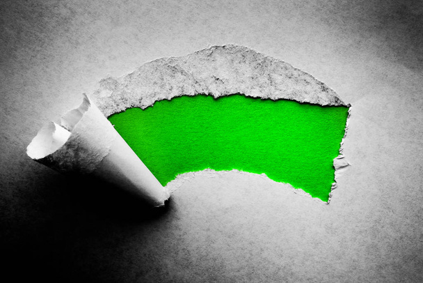 A hole in vintage paper with torn edges close-up with a green vibrant color background inside. - Foto, Imagen