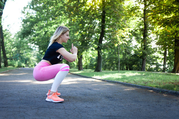 Atraktivní dívka v růžových kamaších dělá dřepy. Sportovní fitness dáma dělá hýždě cvičení - Fotografie, Obrázek