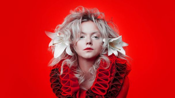 Shades of red. Attractive woman, in a red dress, posing on a red background, with white lily flowers in her hair. - Fotografie, Obrázek