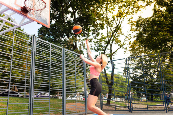 Atletická dívka hodí míč v basketbalovém ringu. Mladá sportovní žena na basketbalovém hřišti - Fotografie, Obrázek