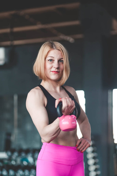  Fitness meisje aan het trainen met een kettlebell in de sportschool. Sportvrouw schudt handen met gewichten - Foto, afbeelding