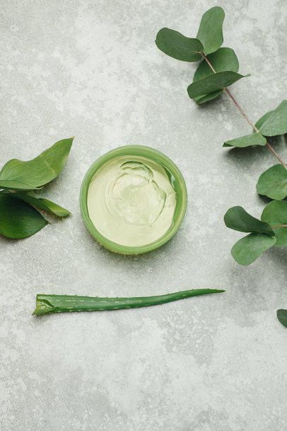 A can of aloe gel next to an aloe branch and eucalyptus leaves. Flat lay. Green aloe gel on a gray background of natural ingredients. The concept of skin care, natural ingredients. aloe vera juice, fr - Photo, Image
