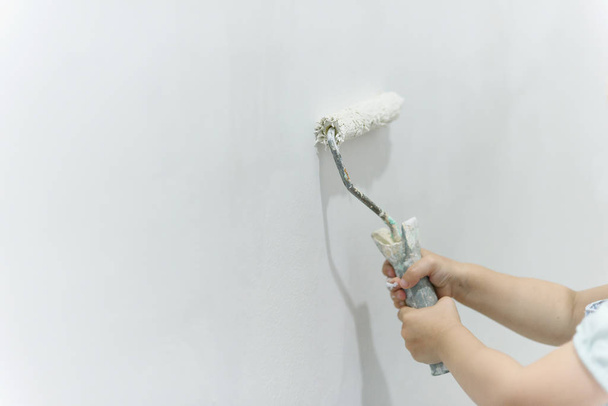 Painting out a white wall with a paint roller with white paint. Close up female hand painting wall with paint roller. - Fotó, kép