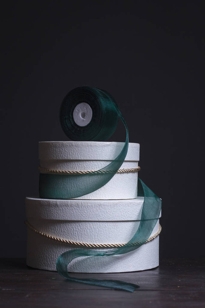 Gros plan de deux boîtes à chapeau rondes blanches et d'un ruban vert sur fond sombre, mise au point sélective
 - Photo, image