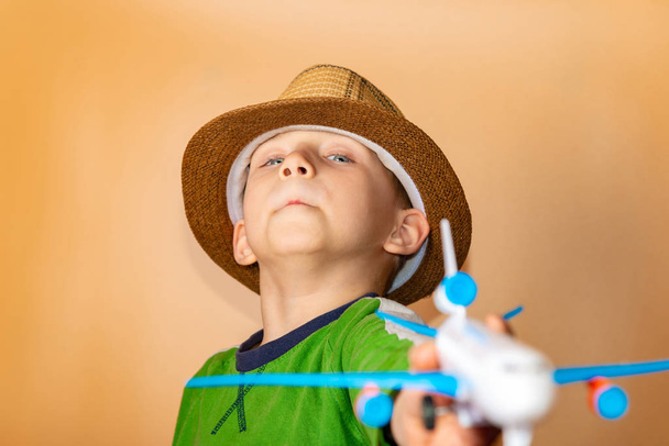 Ένα αγόρι με ψάθινο καπέλο κρατά ένα παιδικό αεροπλάνο στο χέρι του.. - Φωτογραφία, εικόνα