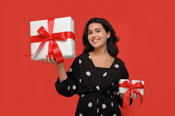 Smiling woman in a black dress choosing between small and big Christmas giftboxes with red ribbon - Photo, image