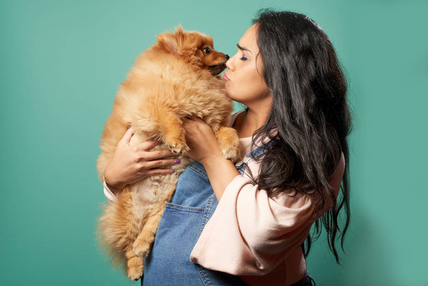 Pregnant brunette woman kisses pug on empty blue background - Fotó, kép