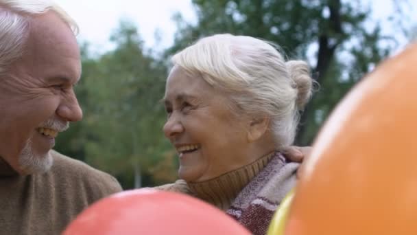 Cheerful mature couple smiling holding air balloons, anniversary celebration - Footage, Video