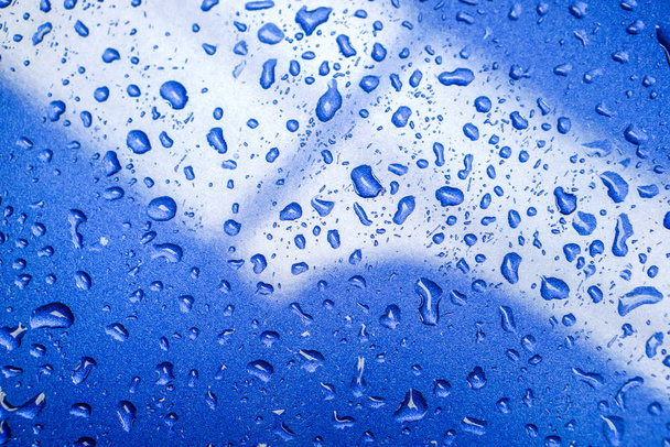 青い車のエンジンフード上の雨滴や反射照明のトップビューの背景とテクスチャ. - 写真・画像