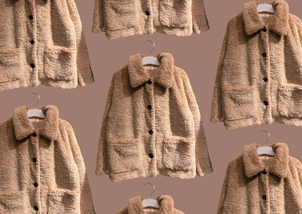 Brown women faux shearling coat on hanger isolated on brown background. Composition of clothes. Flat lay, top view, copy space. Ladies' Trench Coat. Winter clothes pattern. Strict classic white coat - Zdjęcie, obraz