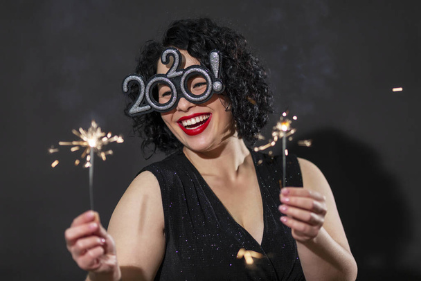 Beautiful laughing plus size girl in evening dress with sparklers. Bright brunette with a festive mood. Black background. Close-up. - Fotó, kép