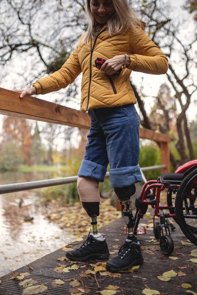 Ένα ανάπηρο κορίτσι χωρίς πόδια παίρνει ένα τηλέφωνο από την τσέπη της.. - Φωτογραφία, εικόνα