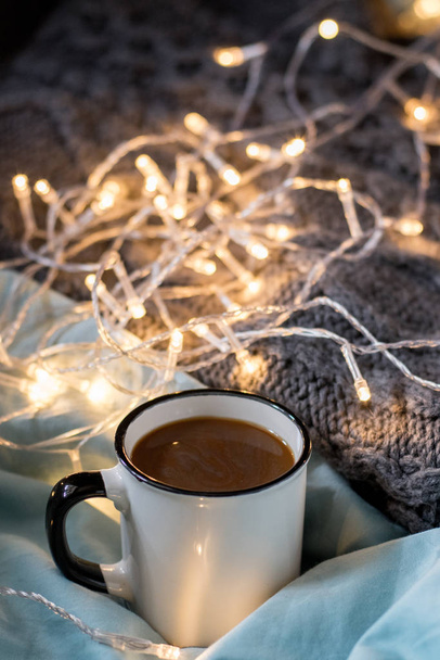 Coffee cup and garland on a bed. Atmospheric hygge style. Cozy w - Photo, Image